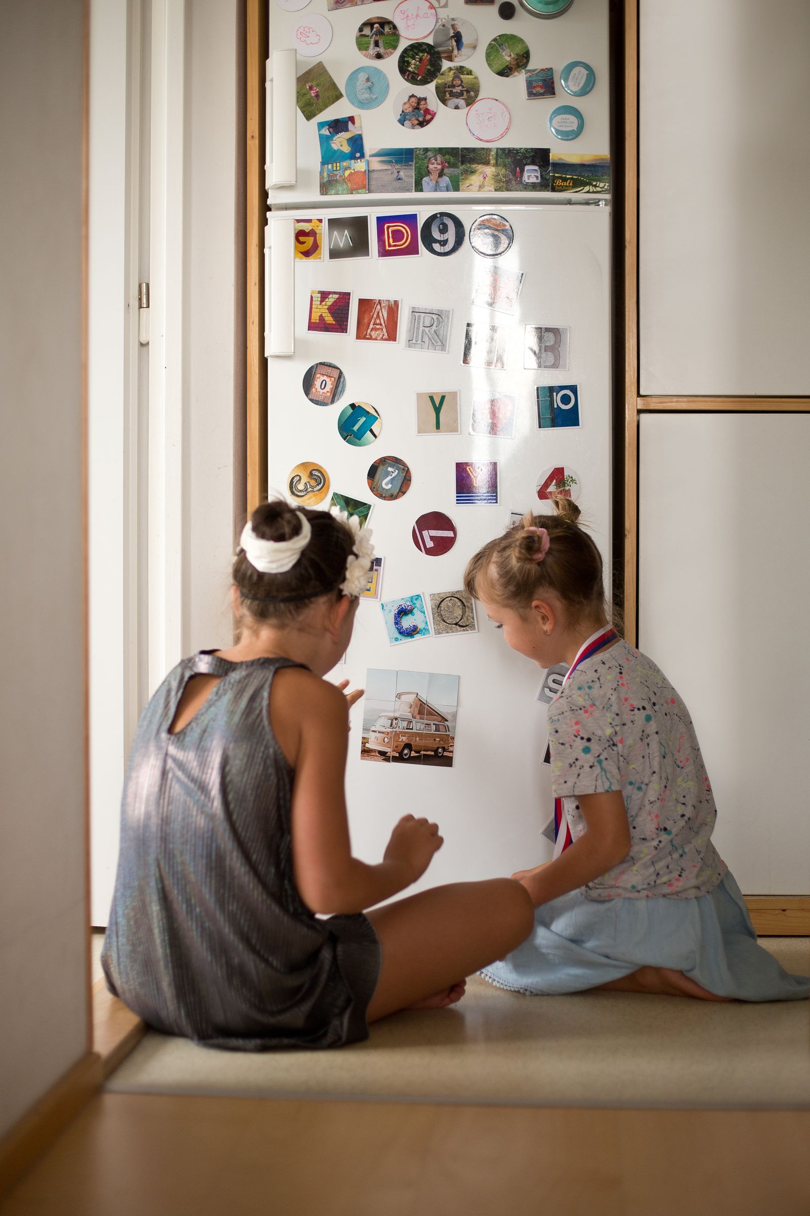 Two girls looking at colourful photo magnets on a fridge